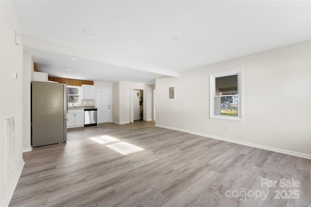 unfurnished living room with light wood-type flooring, a sink, and baseboards