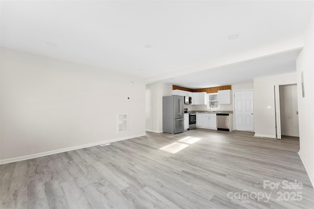 unfurnished living room with a sink, light wood-style flooring, visible vents, and baseboards