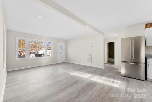 unfurnished living room featuring light wood-style flooring, beam ceiling, visible vents, and baseboards