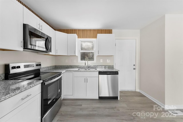 kitchen featuring stainless steel appliances, a sink, white cabinets, light wood-type flooring, and light stone countertops