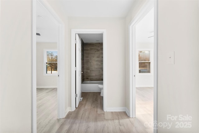 corridor featuring baseboards and light wood finished floors