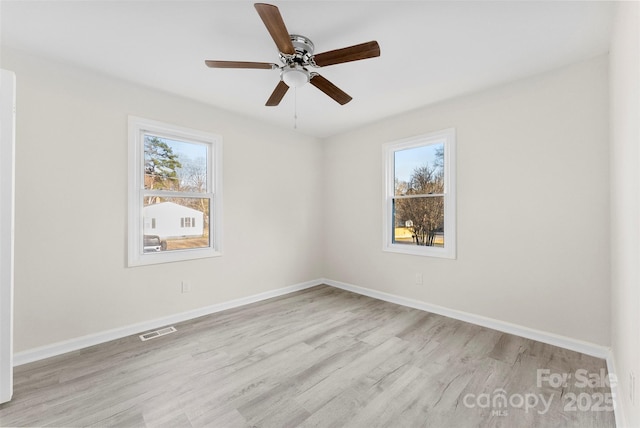 unfurnished room featuring a wealth of natural light, wood finished floors, visible vents, and baseboards