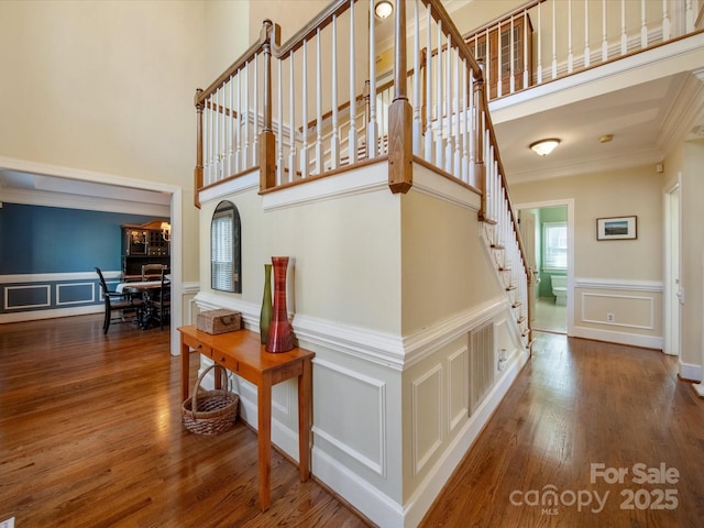 stairs featuring ornamental molding, wood finished floors, a towering ceiling, and a decorative wall