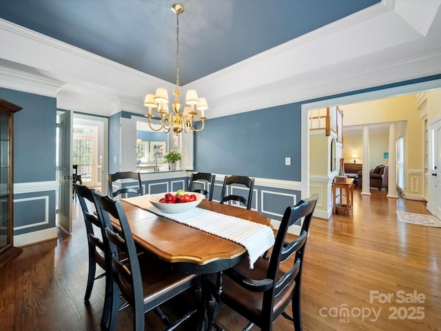 dining area with a wainscoted wall, a notable chandelier, a raised ceiling, a decorative wall, and wood finished floors