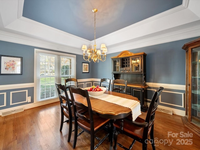 dining room with a wainscoted wall, a tray ceiling, wood-type flooring, and visible vents