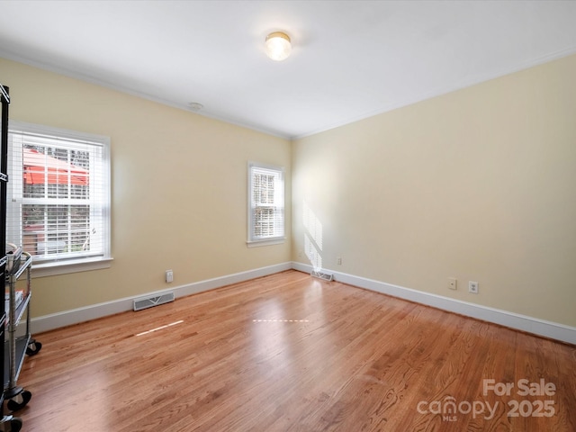 empty room with light wood-type flooring, a healthy amount of sunlight, visible vents, and baseboards