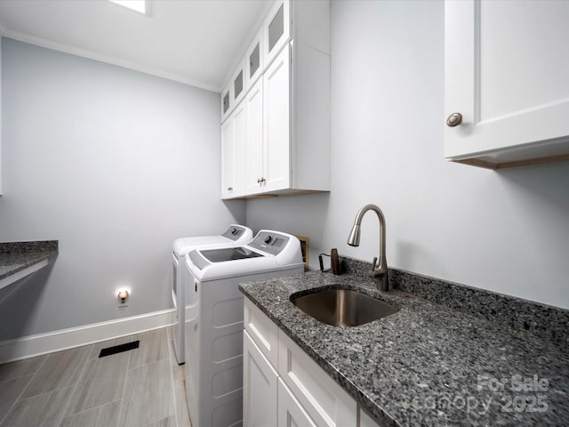 washroom featuring washing machine and clothes dryer, cabinet space, ornamental molding, a sink, and baseboards