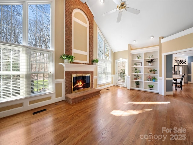 interior space featuring visible vents, a ceiling fan, a brick fireplace, wood finished floors, and high vaulted ceiling