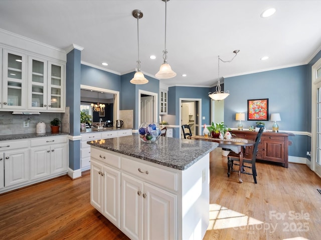 kitchen with glass insert cabinets, a center island, a notable chandelier, and light wood-style flooring