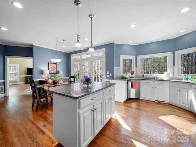 kitchen with light wood finished floors, stainless steel dishwasher, dark stone countertops, and a center island