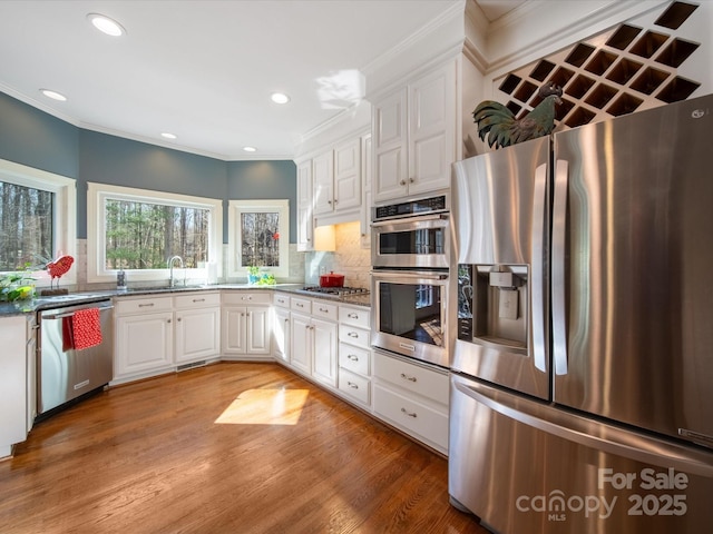 kitchen with crown molding, stainless steel appliances, backsplash, white cabinets, and light wood-type flooring