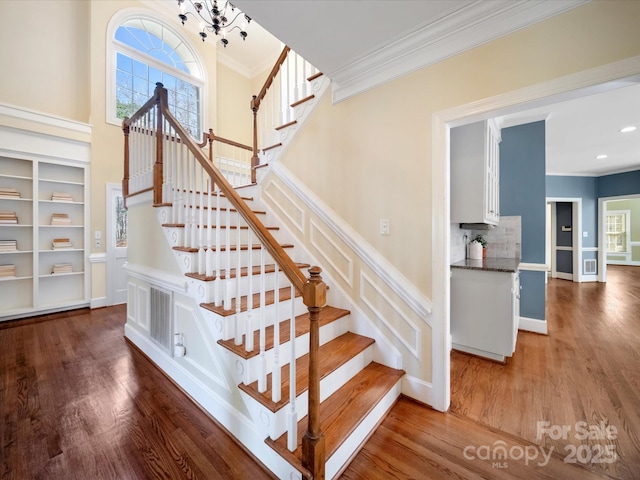 staircase with ornamental molding, visible vents, an inviting chandelier, and wood finished floors