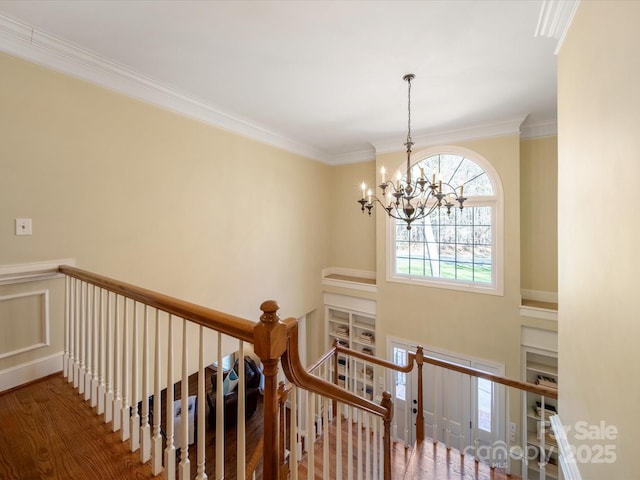 stairway with ornamental molding, an inviting chandelier, and wood finished floors