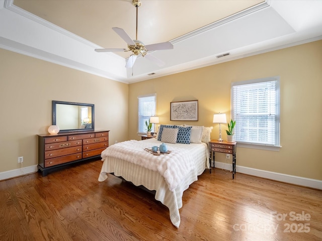 bedroom with wood finished floors, visible vents, baseboards, ornamental molding, and a tray ceiling