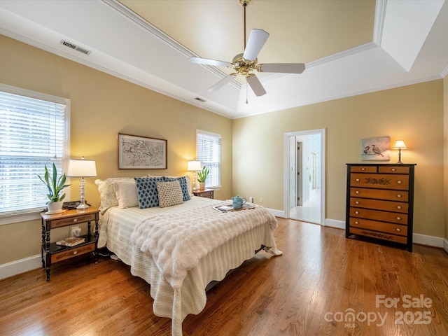 bedroom featuring baseboards, visible vents, ornamental molding, wood finished floors, and a tray ceiling