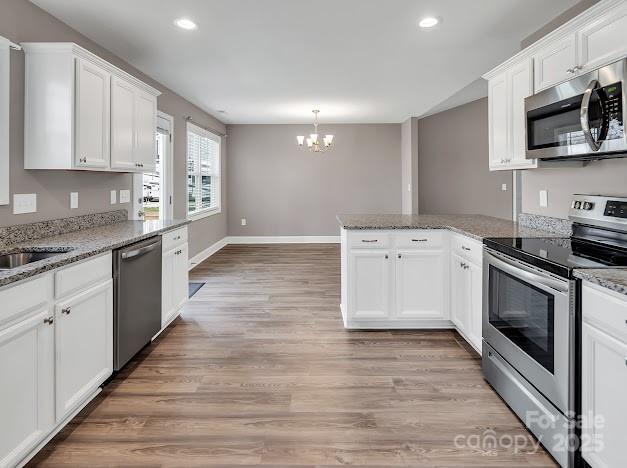 kitchen with white cabinets, light wood-style flooring, a peninsula, an inviting chandelier, and stainless steel appliances