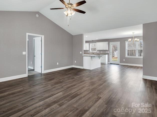 unfurnished living room with lofted ceiling, baseboards, dark wood-style flooring, and ceiling fan with notable chandelier