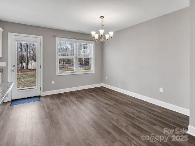 unfurnished dining area featuring an inviting chandelier, baseboards, and dark wood finished floors