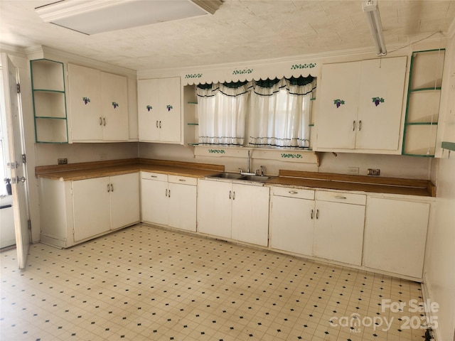 kitchen featuring cream cabinets, a sink, light floors, and open shelves