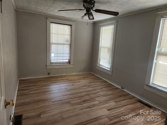 spare room with ceiling fan, visible vents, wood finished floors, and ornamental molding