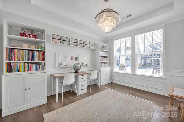 home office with a decorative wall, wood finished floors, visible vents, a raised ceiling, and an inviting chandelier