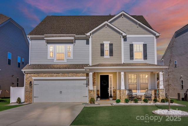 craftsman-style home featuring a porch, driveway, a yard, and stone siding