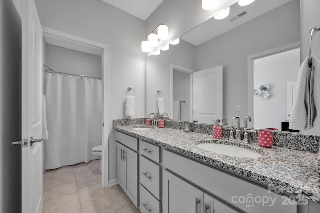 full bath featuring toilet, a sink, visible vents, and double vanity