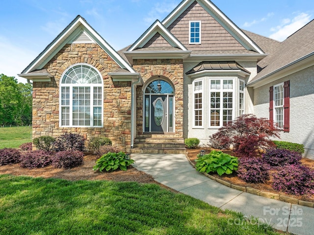 entrance to property featuring a lawn, stone siding, and roof with shingles
