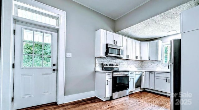 kitchen featuring stainless steel appliances, wood finished floors, baseboards, white cabinets, and decorative backsplash