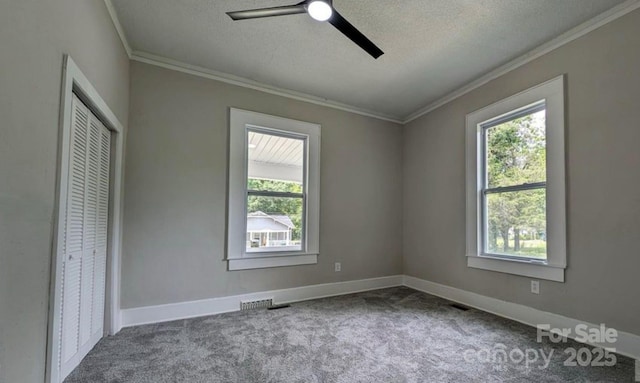carpeted empty room featuring a ceiling fan, crown molding, a textured ceiling, and baseboards