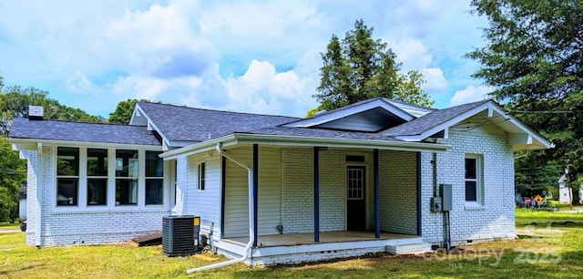 ranch-style home with brick siding, a chimney, covered porch, central air condition unit, and a front yard