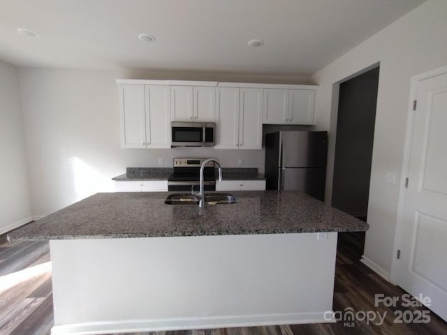 kitchen with stainless steel appliances, a sink, white cabinets, dark stone countertops, and a center island with sink