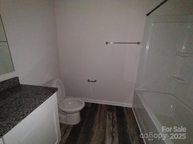 bathroom featuring baseboards, bathing tub / shower combination, toilet, wood finished floors, and vanity