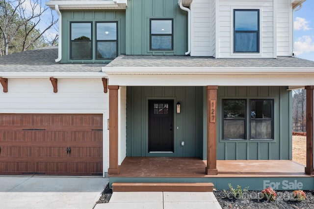 entrance to property featuring covered porch, concrete driveway, a shingled roof, and board and batten siding