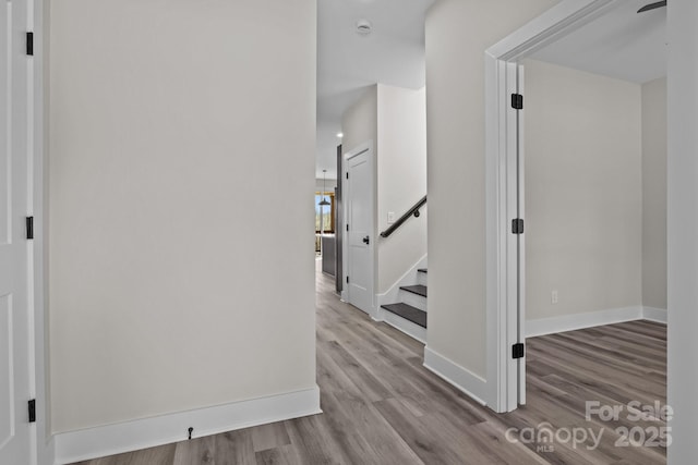 corridor featuring stairs, baseboards, and wood finished floors