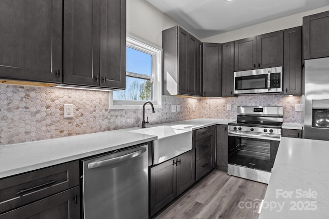 kitchen with decorative backsplash, stainless steel appliances, a sink, and light countertops