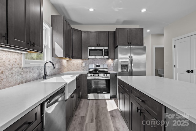 kitchen with light wood finished floors, decorative backsplash, stainless steel appliances, a sink, and recessed lighting