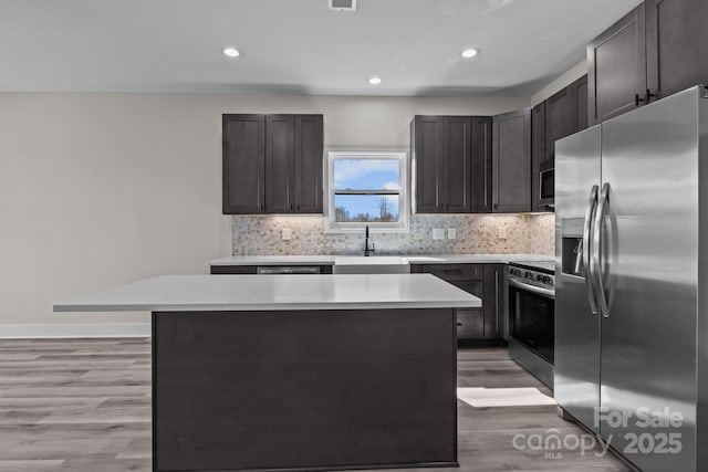 kitchen featuring a kitchen island, light countertops, appliances with stainless steel finishes, backsplash, and light wood finished floors