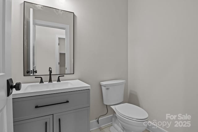 half bathroom featuring baseboards, vanity, and toilet