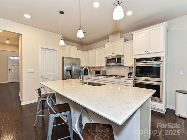 kitchen with light stone counters, dark wood-style flooring, backsplash, appliances with stainless steel finishes, and a sink