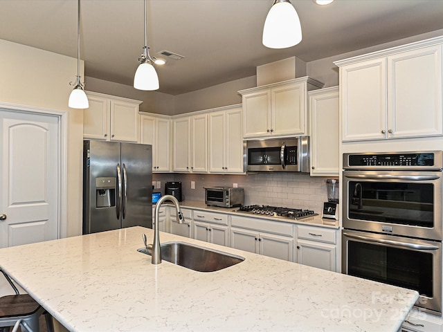 kitchen with stainless steel appliances, a sink, visible vents, hanging light fixtures, and tasteful backsplash