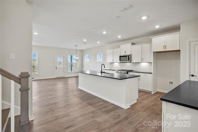 kitchen featuring dark countertops, stainless steel microwave, a sink, and visible vents