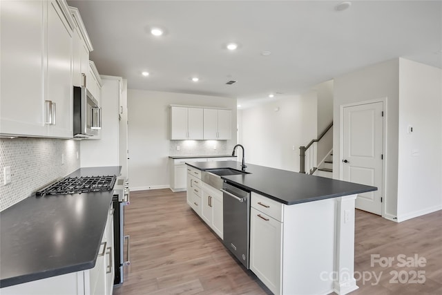 kitchen featuring dark countertops, light wood-style floors, stainless steel appliances, and a sink