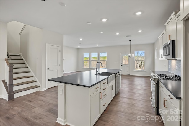 kitchen with stainless steel appliances, dark countertops, decorative backsplash, a sink, and wood finished floors