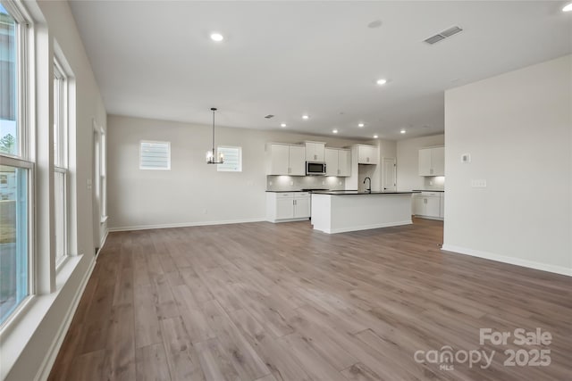 unfurnished living room featuring recessed lighting, a sink, visible vents, baseboards, and light wood-type flooring