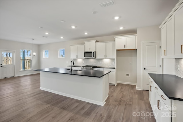 kitchen with visible vents, dark countertops, stainless steel microwave, stove, and a sink