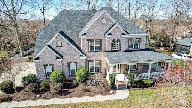 view of front of home with covered porch, a front lawn, and brick siding