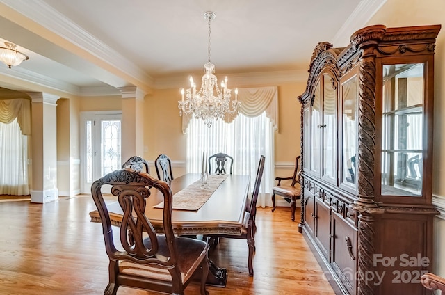 dining room with crown molding, light wood-type flooring, decorative columns, and an inviting chandelier