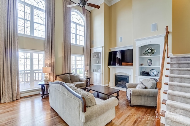 living area with visible vents, a fireplace with flush hearth, stairway, wood finished floors, and built in shelves