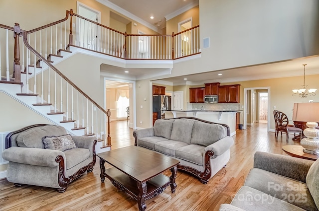 living area featuring ornamental molding, light wood finished floors, stairway, and a notable chandelier